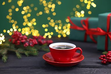 Fincanda romatik kahve, hediye kutuları ve siyah ahşap masadaki Noel dekoru ile bulanık ışıklı yeşil arka plan, yakın çekim. Bokeh etkisi