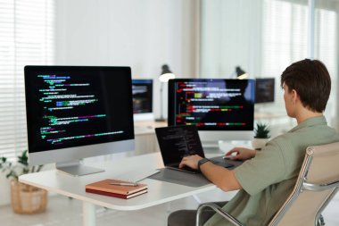 Ofisteki beyaz masada bilgisayar ve dizüstü bilgisayar üzerinde çalışan programcı