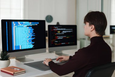 Ofisteki beyaz masada çift monitörlü bilgisayar üzerinde çalışan programcı