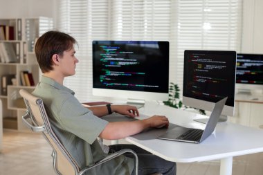 Ofisteki beyaz masada bilgisayar ve dizüstü bilgisayar üzerinde çalışan programcı