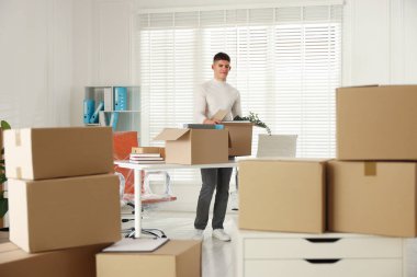 Taşınma günü. Genç adam ofisteki karton kutulara farklı eşyalar koyuyor.