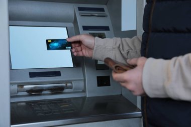 Banka kartı ve cüzdanı olan bir adam modern para makinesini kullanıyor, yakın plan. ATM