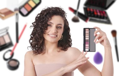 Beyaz arka planda düşen dekoratif kozmetiklere karşı göz falı olan güzel bir makyaj sanatçısı.