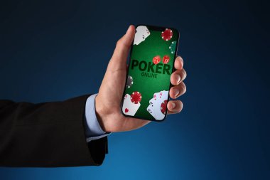 Koyu mavi arkaplanda cep telefonuyla online poker oynayan adam, yakın plan