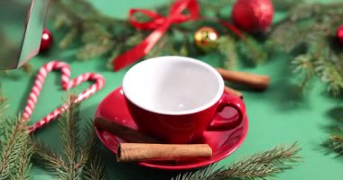 Yeşil arka planda fincana aromatik kahve, tarçın ve Noel dekoru dökülüyor. Yakın plan.