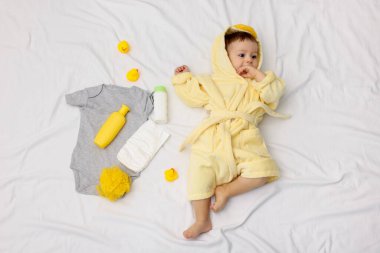 Bornozlu şirin bir bebek, banyodaki aksesuarlar ve giysiler, üst manzara.