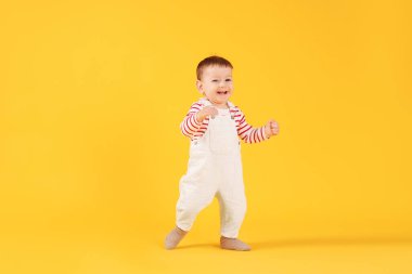 İlk adımlar. Sarı arka planda yürüyen şirin bir bebek.