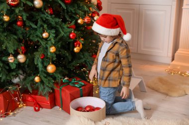Noel Baba şapkalı küçük çocuk evde Noel ağacı süslüyor.