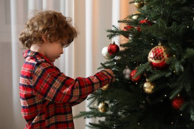 Pijamalı küçük çocuk evde Noel ağacı süslüyor.