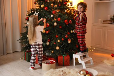 Pijamalı çocuklar evde Noel ağacı süslüyorlar.