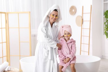 Anne ve kız göz bantlı ve banyoda bornoz giyen saçları sarılı.