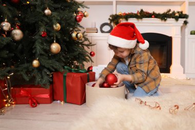 Noel Baba şapkalı küçük çocuk evde Noel ağacı süslüyor.