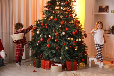 Pijamalı çocuklar evde Noel ağacı süslüyorlar.