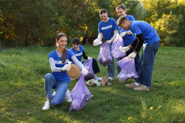 Çantalı bir grup mutlu gönüllü parkta çöp topluyor.