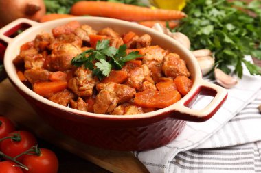 Pişirme kabında nefis pişirilmiş güveç ve masada taze malzemeler, yakın plan.