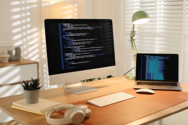 Ofisteki ahşap masada bilgisayar, dizüstü bilgisayar ve kulaklık ile programcının işyeri