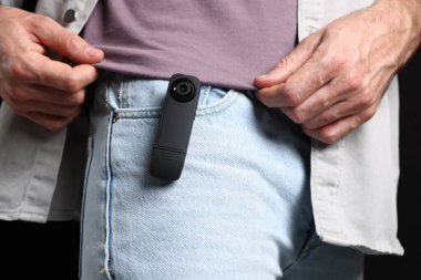 Cebinde siyah arka planda gizli kamera olan adam, yakın plan.