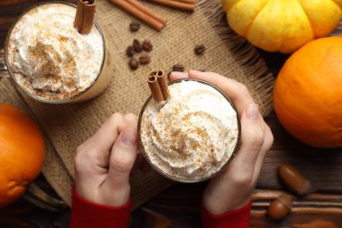 Ahşap masada kremalı balkabaklı latte tutan bir kadın.