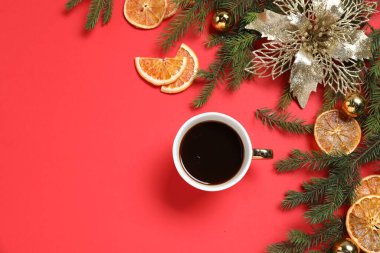 Bir fincan aromatik kahve, köknar ağacı dalları ve kırmızı arka planda Noel dekoru olan düz bir kompozisyon. Metin için boşluk