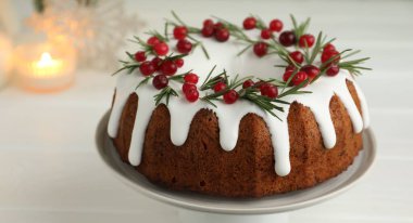 Beyaz ahşap masada kremalı, kızılcıklı ve biberiyeli lezzetli bir Noel pastası.