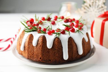Beyaz ahşap masada kremalı, kızılcıklı ve biberiyeli lezzetli bir Noel pastası.