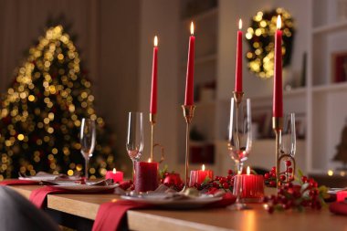 Şenlikli bir odada tabaklar, bardaklar ve yanan mumlarla süslü bir Noel sofrası. Bokeh etkisi