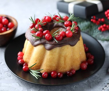 Çikolata kaplı lezzetli Noel pastası, yaban mersini ve biberiyeli gri desenli masa, yakın plan.