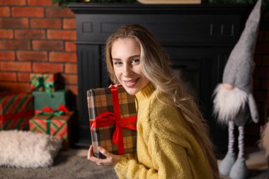 Evinde süslü şöminenin yanında Noel hediyesi olan güzel bir kadın.