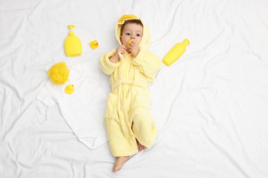 Yatakta banyo aksesuarları ve bornozlu şirin bir bebek.