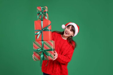 Yeşil arka planda bir sürü hediye kutusu olan, Noel Baba şapkalı gülümseyen kadın. Noel ve Yeni Yıl Kutlaması