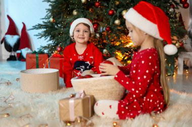 Noel Baba şapkalı şirin çocuklar Noel ağacının yanında süsleniyorlar, seçici bir şekilde odaklanıyorlar.