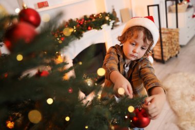 Noel Baba şapkalı küçük çocuk evde Noel ağacı süslüyor. Bokeh etkisi
