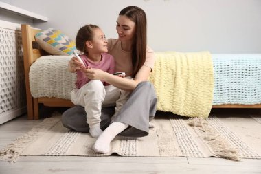 Diyabet. Gülümseyen anne evde yatağın yanında mızrak kalemle kızının kan şekerini ölçüyor.