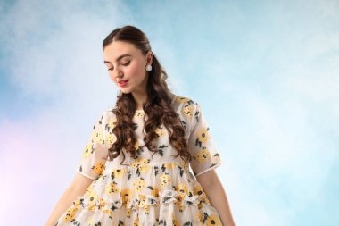 Açık mavi arka planda, dumanlı, güzel giyimli genç bir kadın.