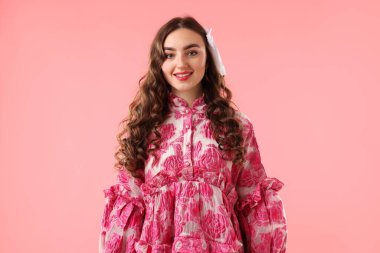 Pembe arka planda güzel giyimli genç bir kadın.