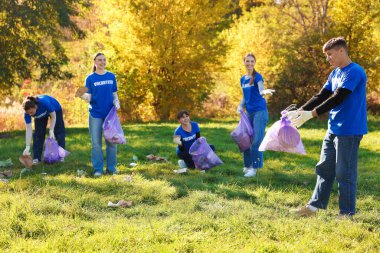 Çantalı bir grup mutlu gönüllü parkta çöp topluyor.