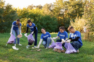 Çantalı bir grup mutlu gönüllü parkta çöp topluyor.