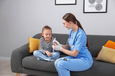 Diyabet. Tıbbi eldivenli doktor, küçük kızın kan şekeri seviyesini kanepedeki kanepede neşterle ölçüyor.