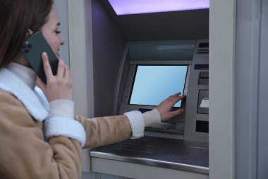 Telefonla konuşurken para makinesi kullanan bir kadın. ATM