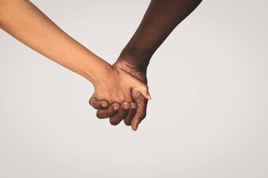 Kadın ve Afrikalı Amerikalı erkek açık gri arka planda el ele tutuşuyorlar, yakın plan.