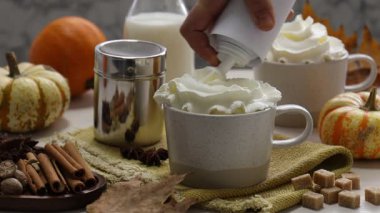 Beyaz masada balkabaklı latteye krema ve tarçın ekleyen kadın, yakın plan.