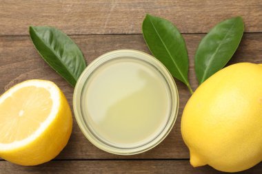 Tabakta limon suyu, yapraklar ve ahşap masada taze limonlar.