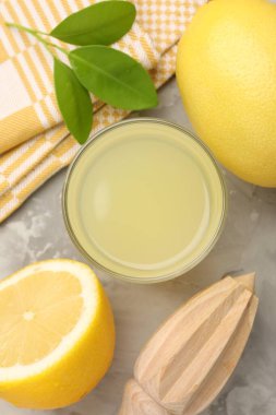 Bardakta limon suyu, sıkma, yapraklar ve açık gri masada taze limonlar.