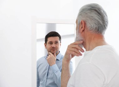 Kıdemli adam aynada kendini genç görüyor. Kişilik kavramı, geçmiş ve gelecek, zaman akışı, yaş