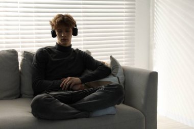 Evdeki kanepede kulaklık takan depresyondaki genç çocuk.