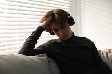 Evdeki kanepede kulaklık takan depresyondaki genç çocuk.