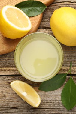 Bardakta limon suyu, yapraklar ve ahşap masada taze limonlar.
