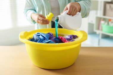 Kadın plastik bir leğene deterjan döküyor. İçerideki ahşap masada giysileri var. Yakın plan.