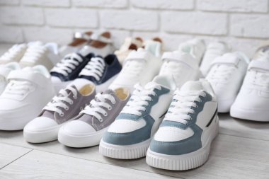 Beyaz tuğla duvarın yanında, gri ahşap zeminde birçok şık çocuk ayakkabısı var.