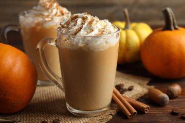 Cam bardaklarda krema ve ahşap masada malzemelerle birlikte lezzetli balkabaklı latte.